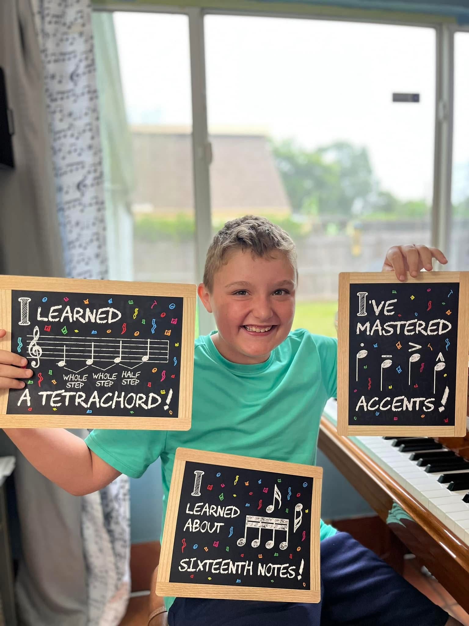 Young student proudly holding chalkboards showing music theory milestones