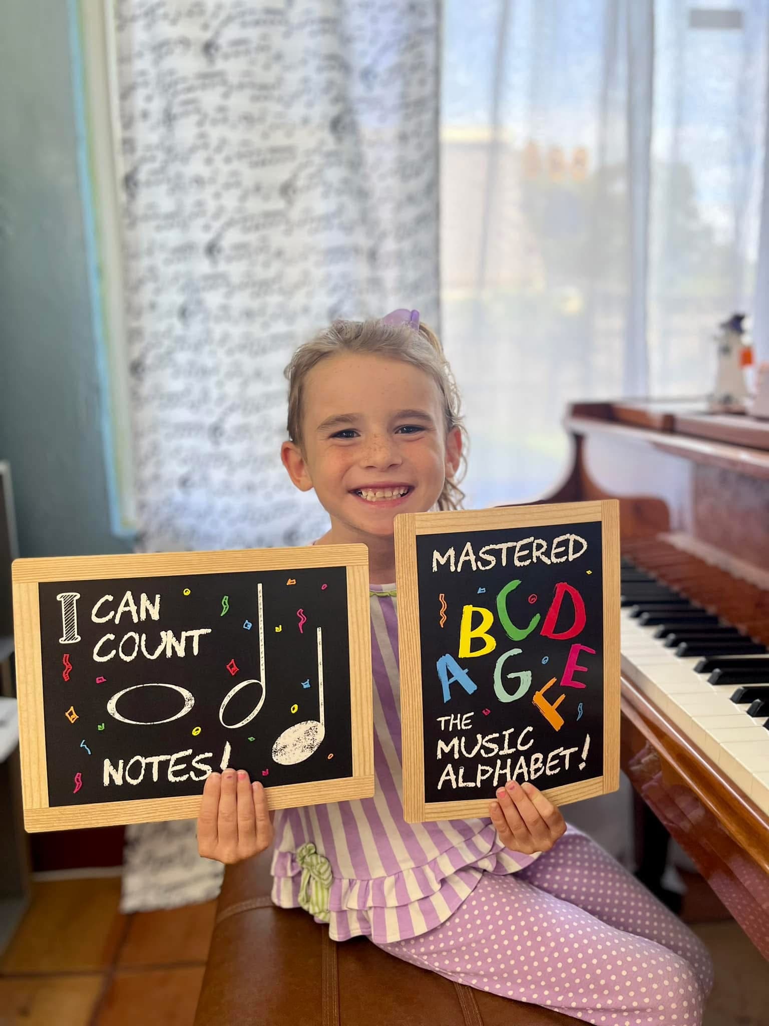 Young girl holding chalkboards showing she learned to count notes and mastered the music alphabet