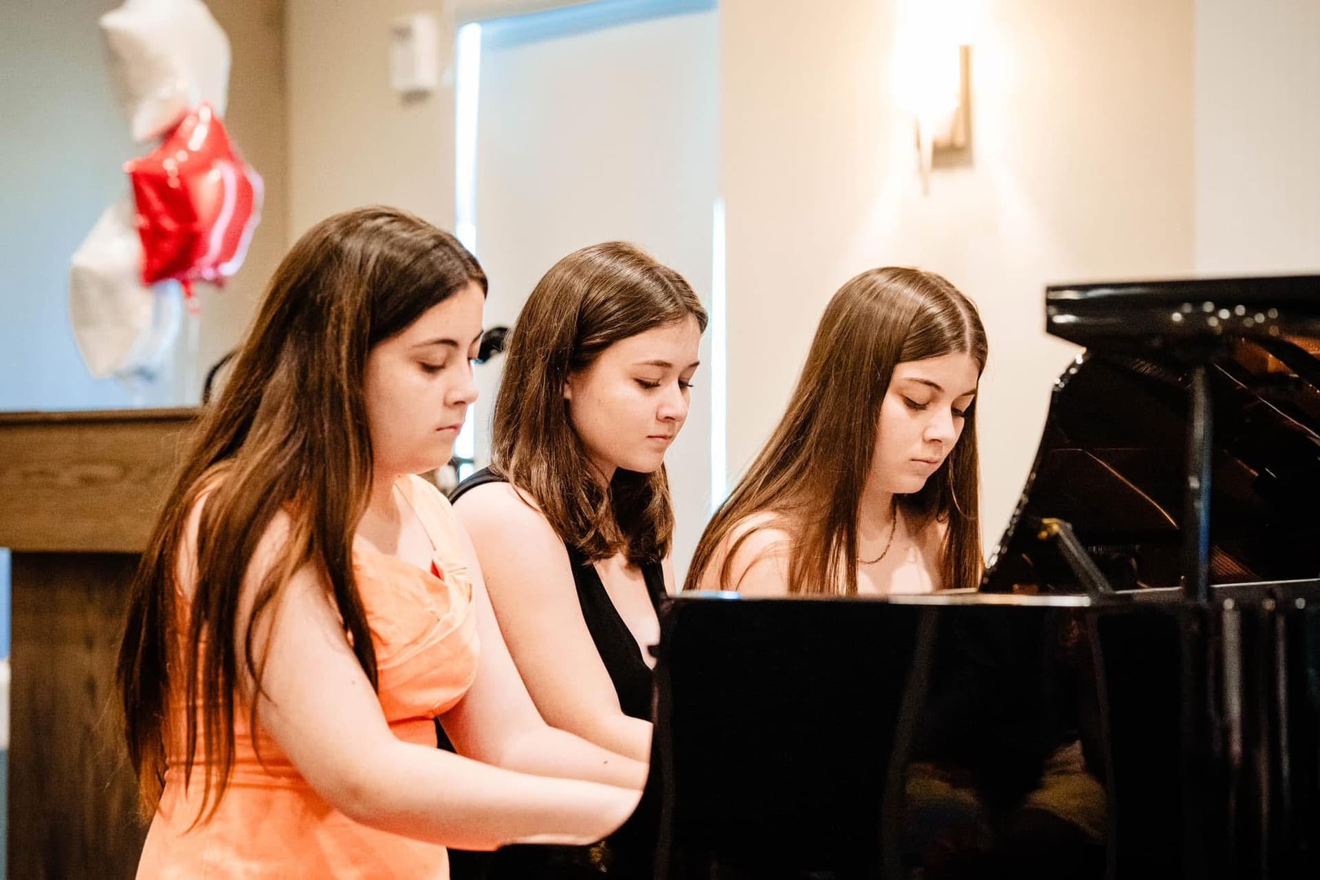 Three students performing together at the piano